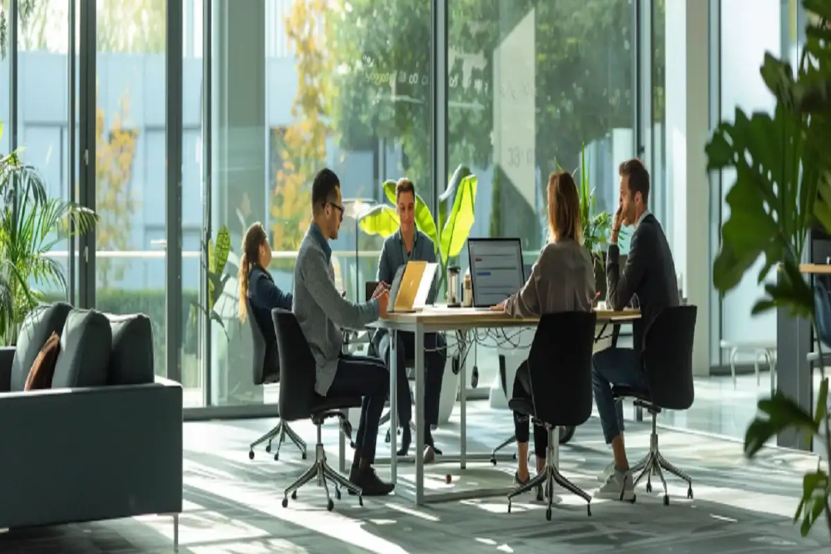 Employees collaborate at a large table in a sunlit, modern office, illustrating how top enterprise search software enables streamlined information retrieval and boosts productivity.